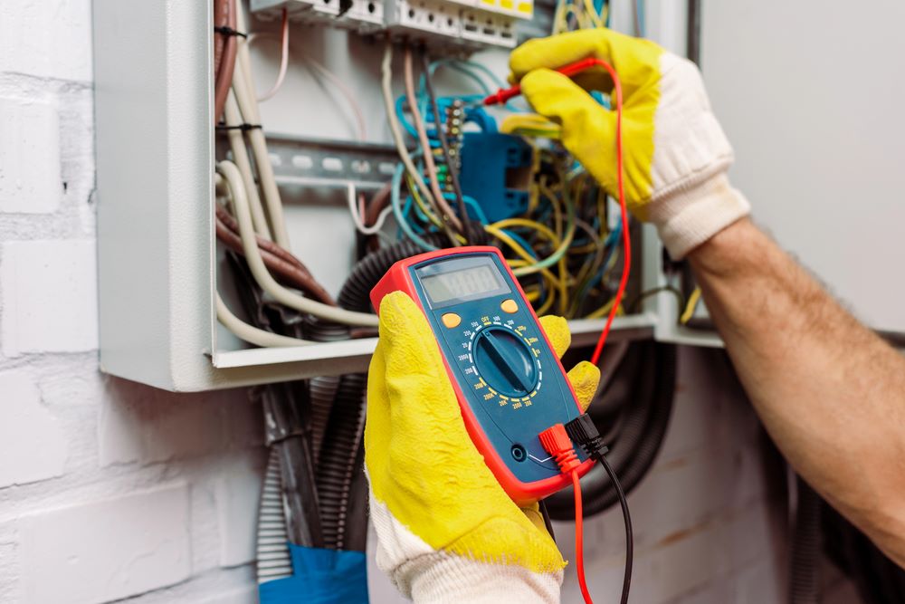 Image of a cropped view of a workman in gloves using a multimeter, featuring Hero Service Pros and highlighting services built around the way electricians work.