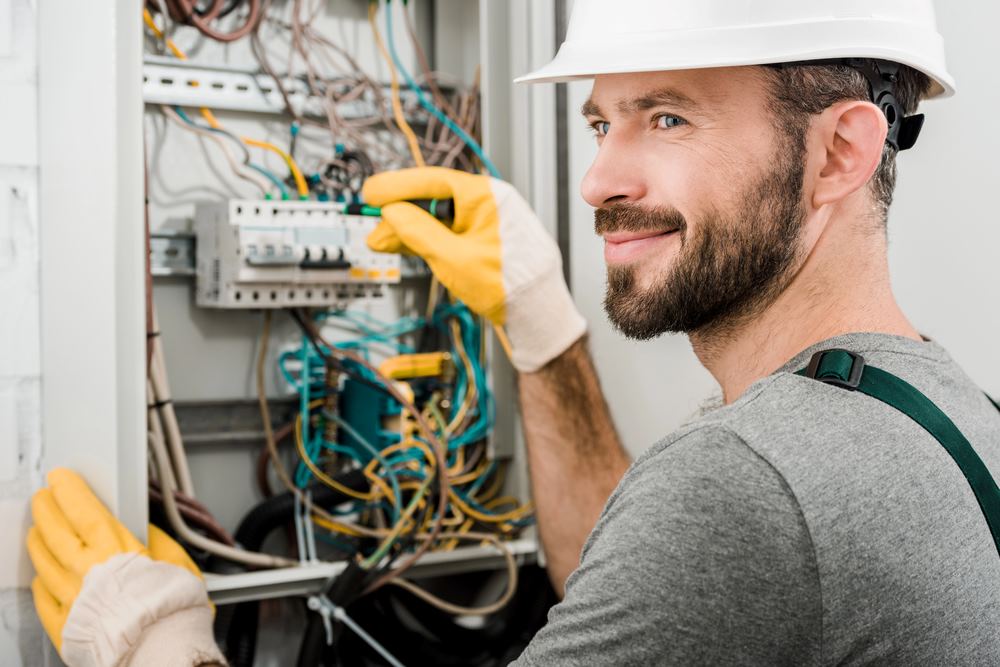 Image of a cheerful electrician repairing an electrical box, featuring Hero Service Pros and highlighting how to get more done with less hassle through expert electrical services.