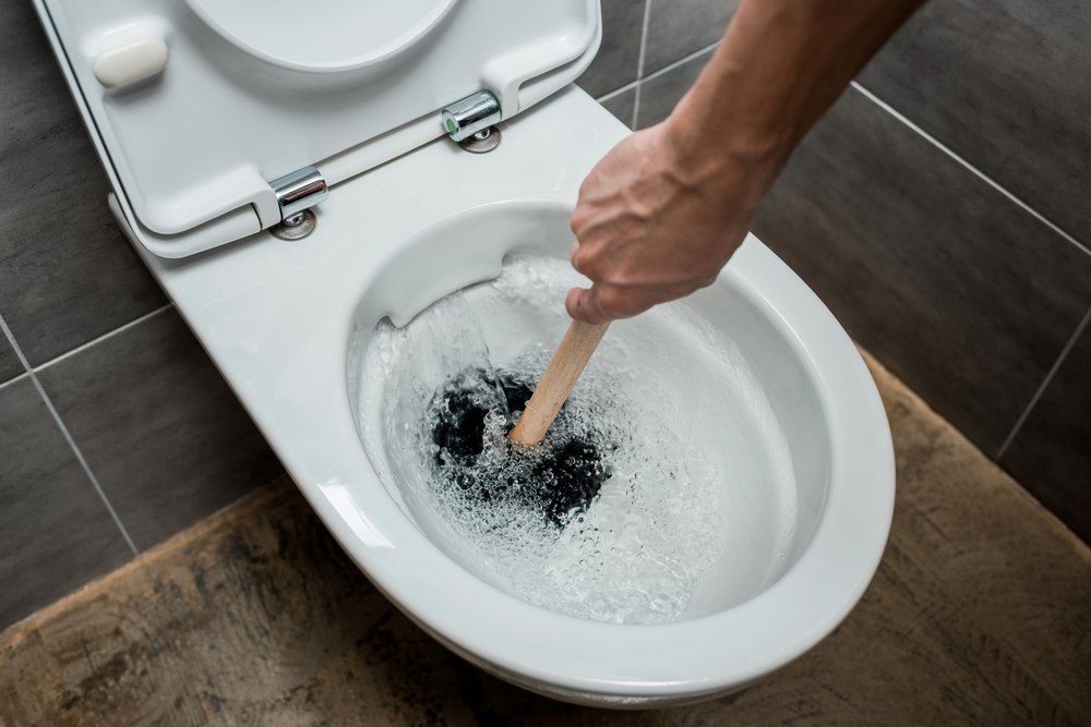 Image of a cropped view of a plumber using a plunger in a toilet bowl, featuring Hero Service Pros and highlighting strategies to make your plumbing business the go-to choice for customers.