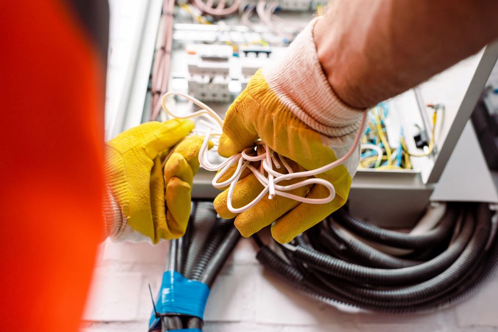 Image of a cropped view of an electrician wearing gloves and holding wires, featuring Hero Service Pros and highlighting support services designed to grow with your electrical business.